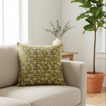 Load image into Gallery viewer, An olive green throw pillow with a white and blue floral vine pattern, resting on a dark blue shipping box over a rustic wooden floor.
